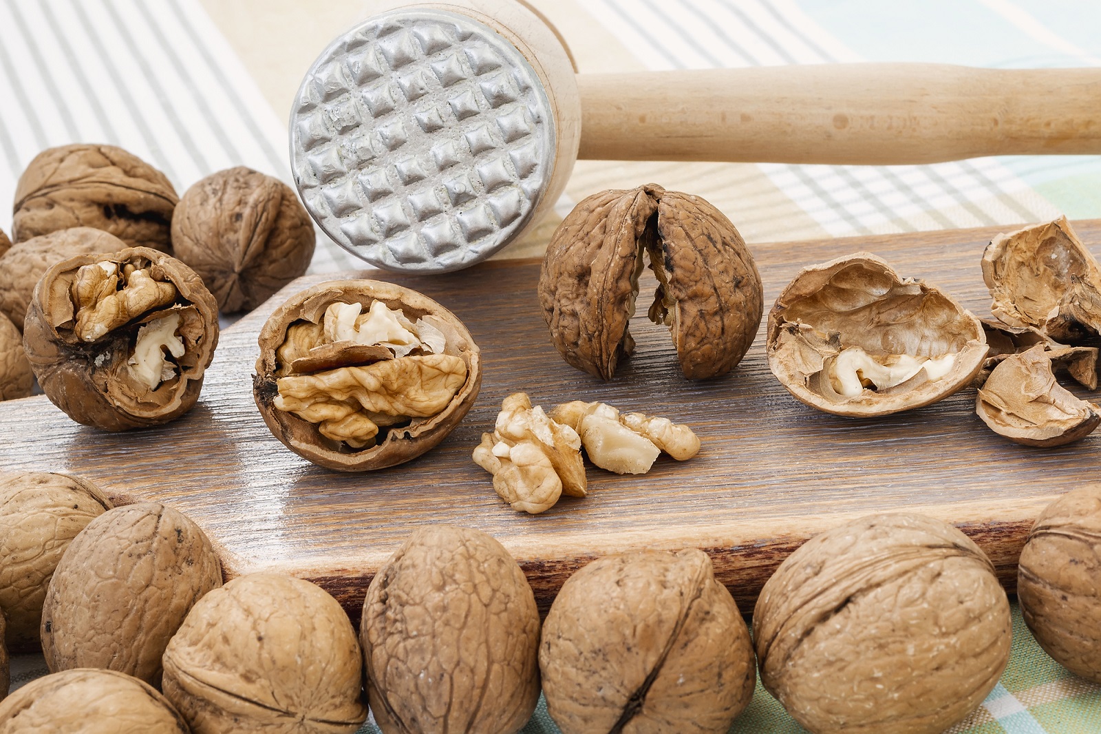 Front view of whole and cracked walnuts (Juglans regia) near wooden meat mallet on a brown wooden board. Natural unbleached nuts. Vegetarian food.